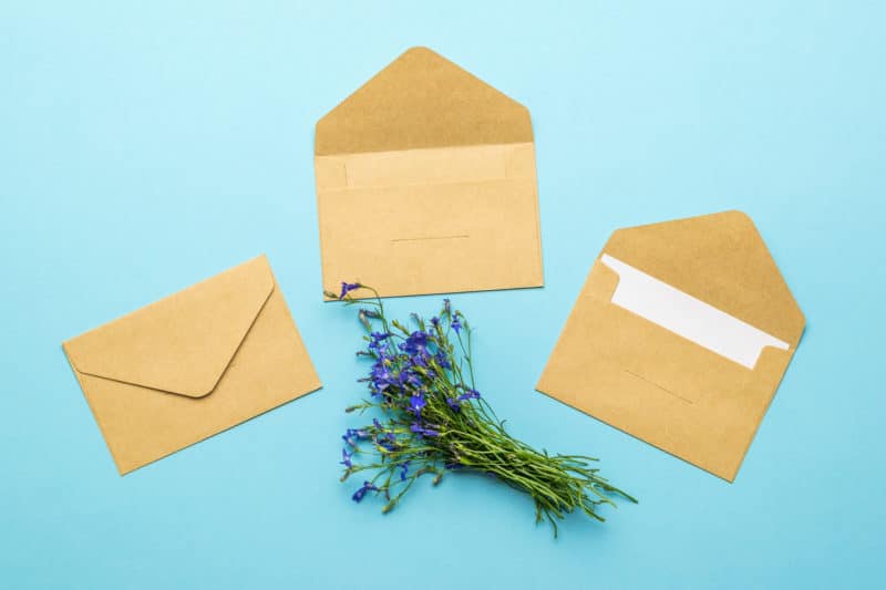 three paper envelopes letters bouquet flowers blue background flat lay